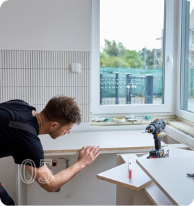 A man working on a kitchen counter installation, using a drill near a window.