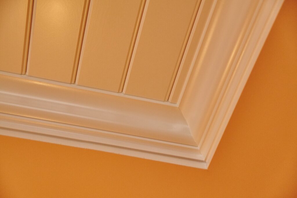 A close-up of a ceiling with wood paneling and white molding against an orange wall.