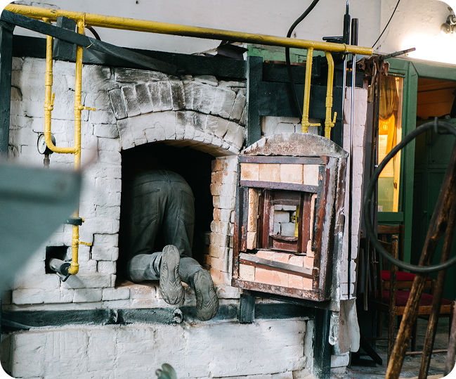 A person working inside a kiln, with only their legs visible, engaged in maintenance or repair.